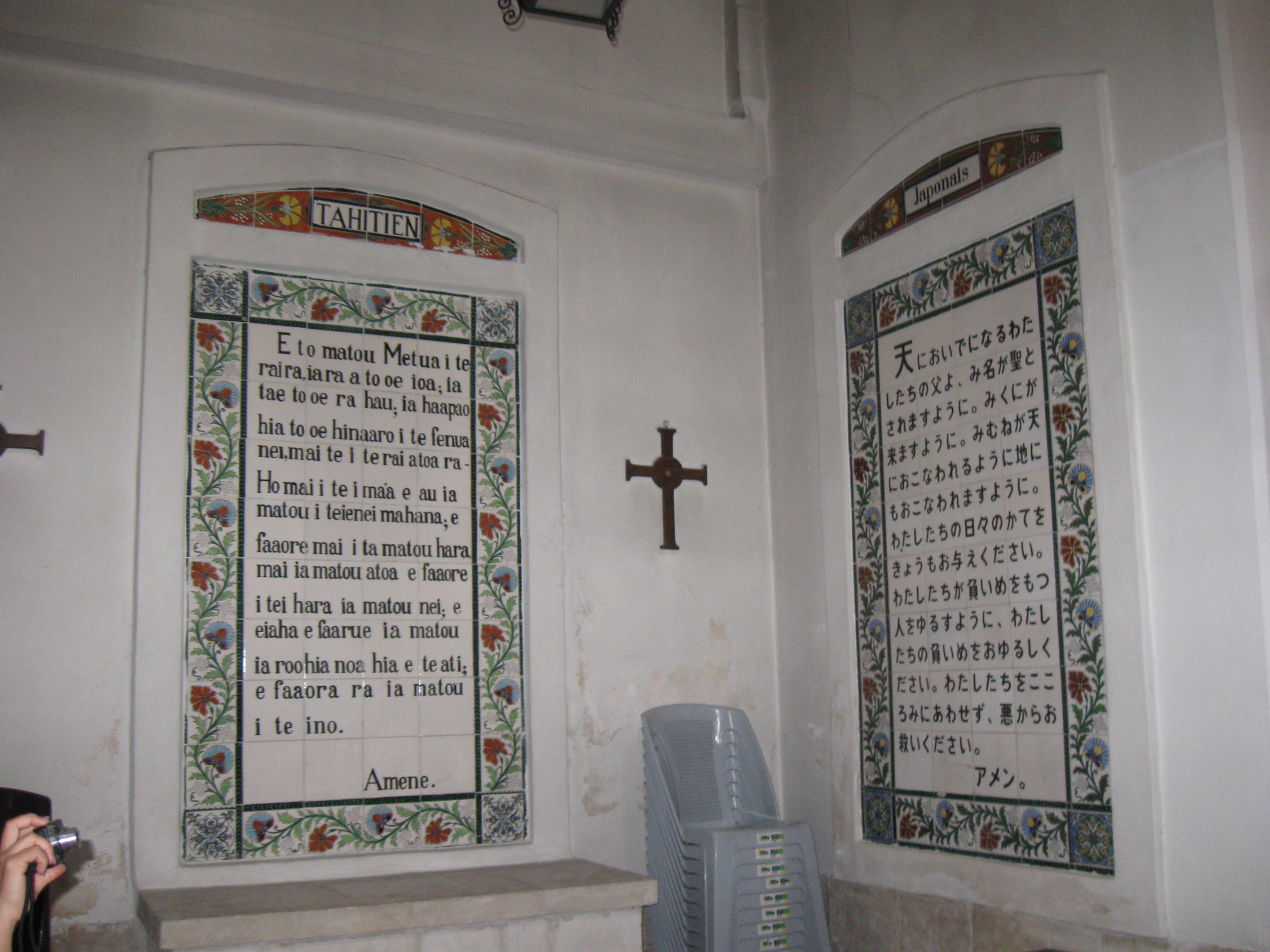 Photo of two plaques on a wall. On the left is a text of the Lord's Prayer in Tahitian; on the right is the text in Japanese. A cross hangs on the wall between them.